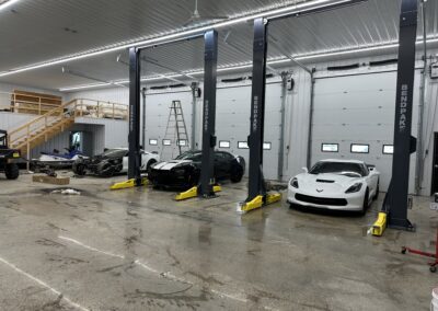 A car repair shop with two cars parked on the floor, tools hanging on the walls, and mechanics working on engines.