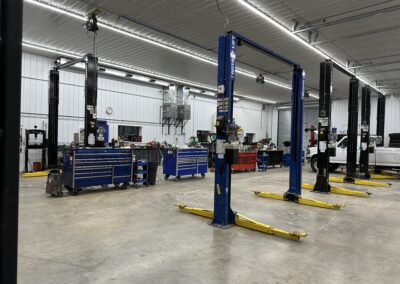 Inside a car repair shop, two cars parked on the floor, with mechanics inspecting engines and tools neatly organized.